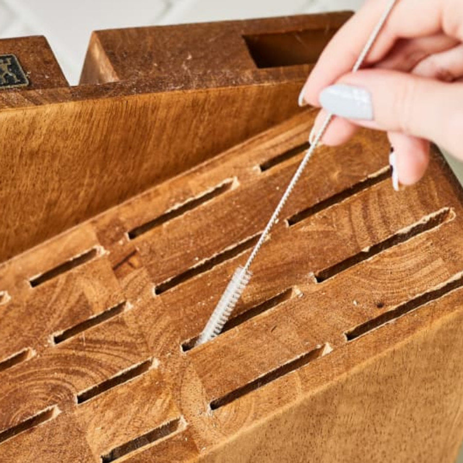 Cleaning crumbs out of the narrow slots of a wooden knife block with a brush