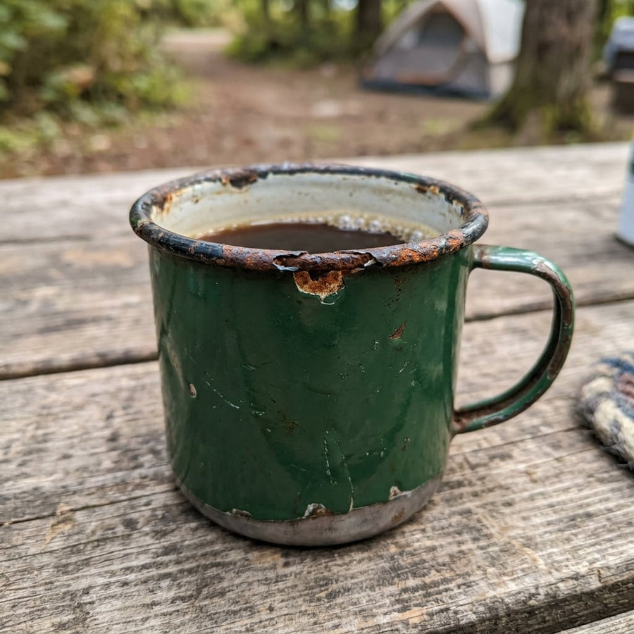 Dented, chipped enamel camping mug with rust around the rim