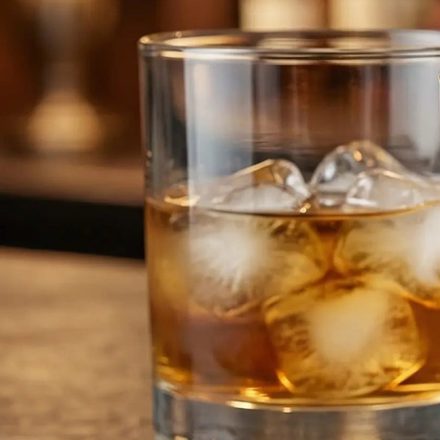 Glass of whiskey with ordinary ice cubes melting into a puddle on the bar - watered-down drink