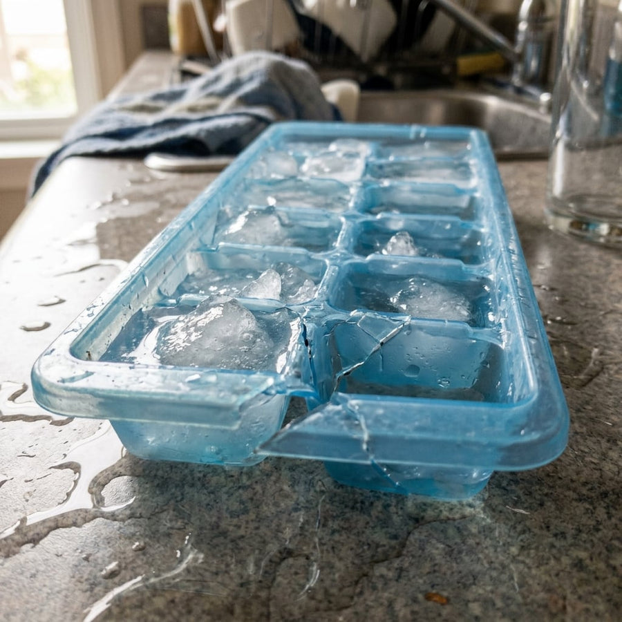 Cracked plastic ice cube tray with half-melted ice and puddles of water