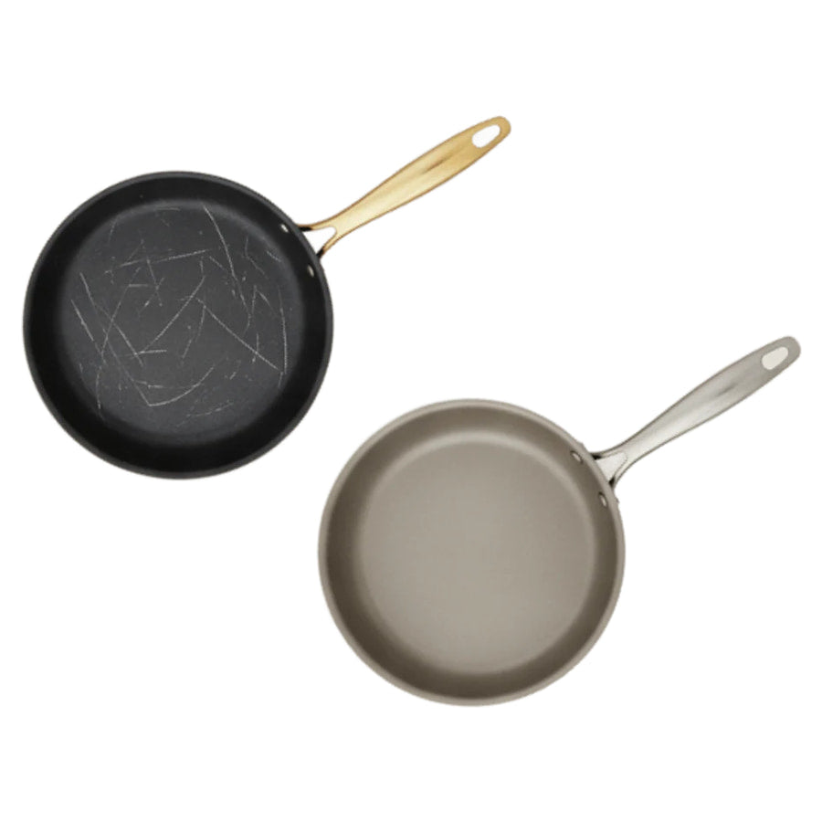 A scratched nonstick pan next to a worn aluminum pan