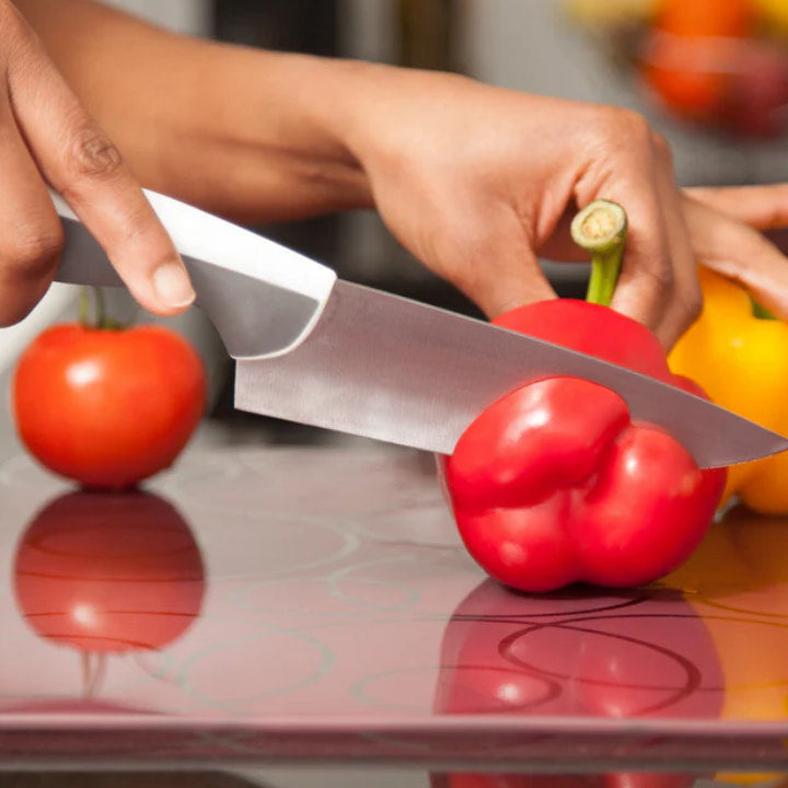 Knife slicing a red pepper on a glass cutting board - hard glass surfaces dull knife edges